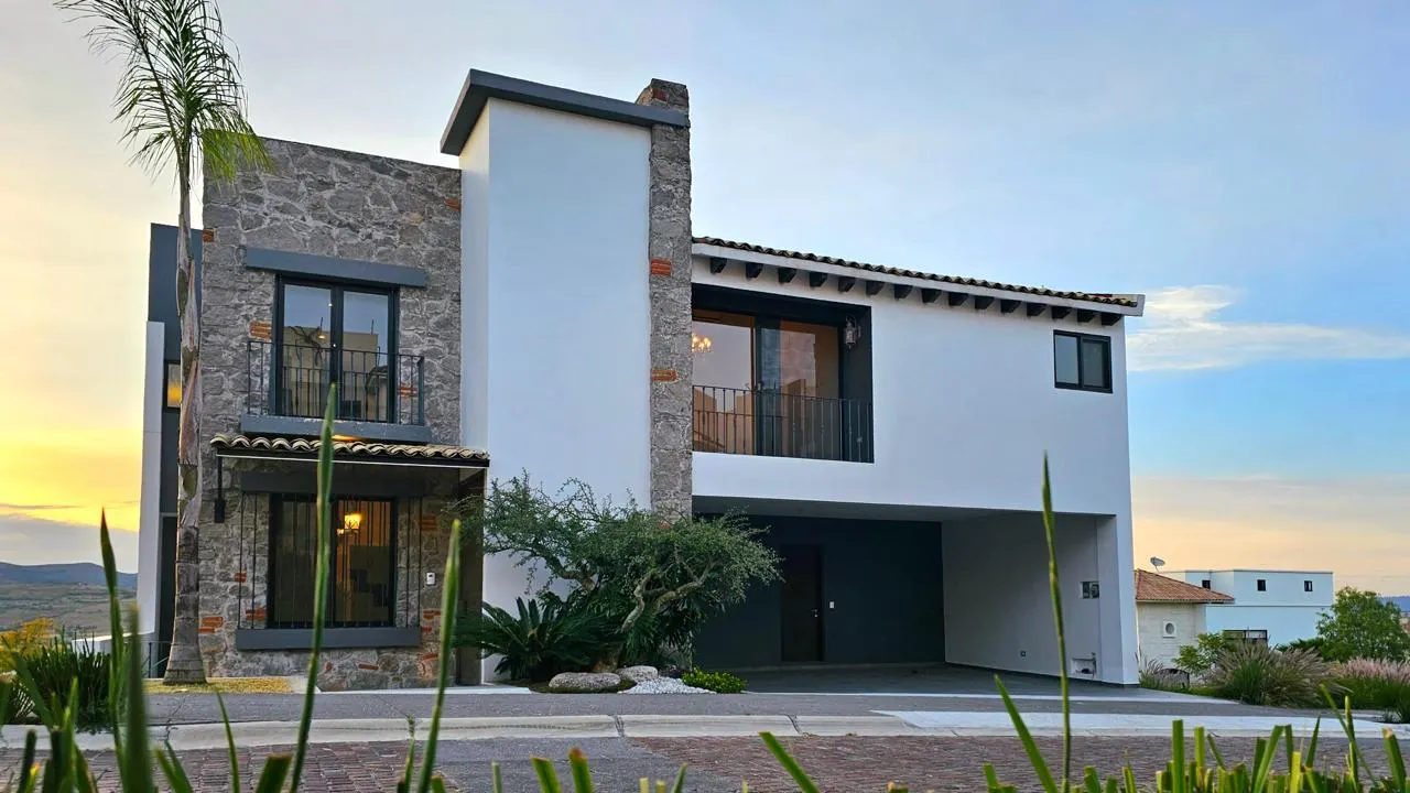 Fachada de la casa a última hora de la tarde, con muro de piedra y cubierta a dos aguas.