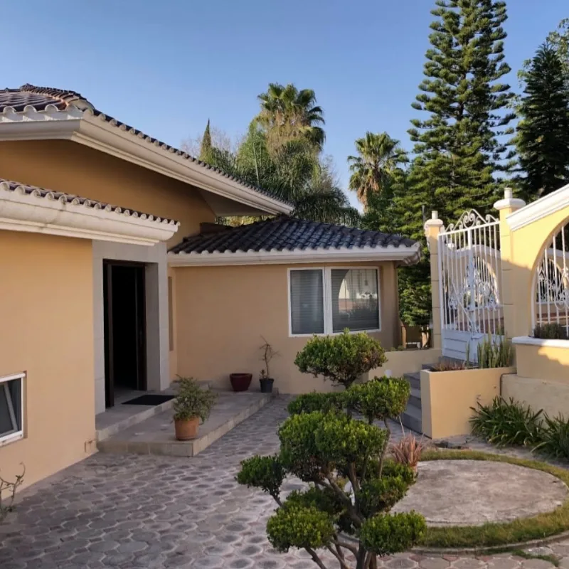 Fachada de la residencia La Concepción, con cubierta de teja, jardín y reja de herrería blanca.