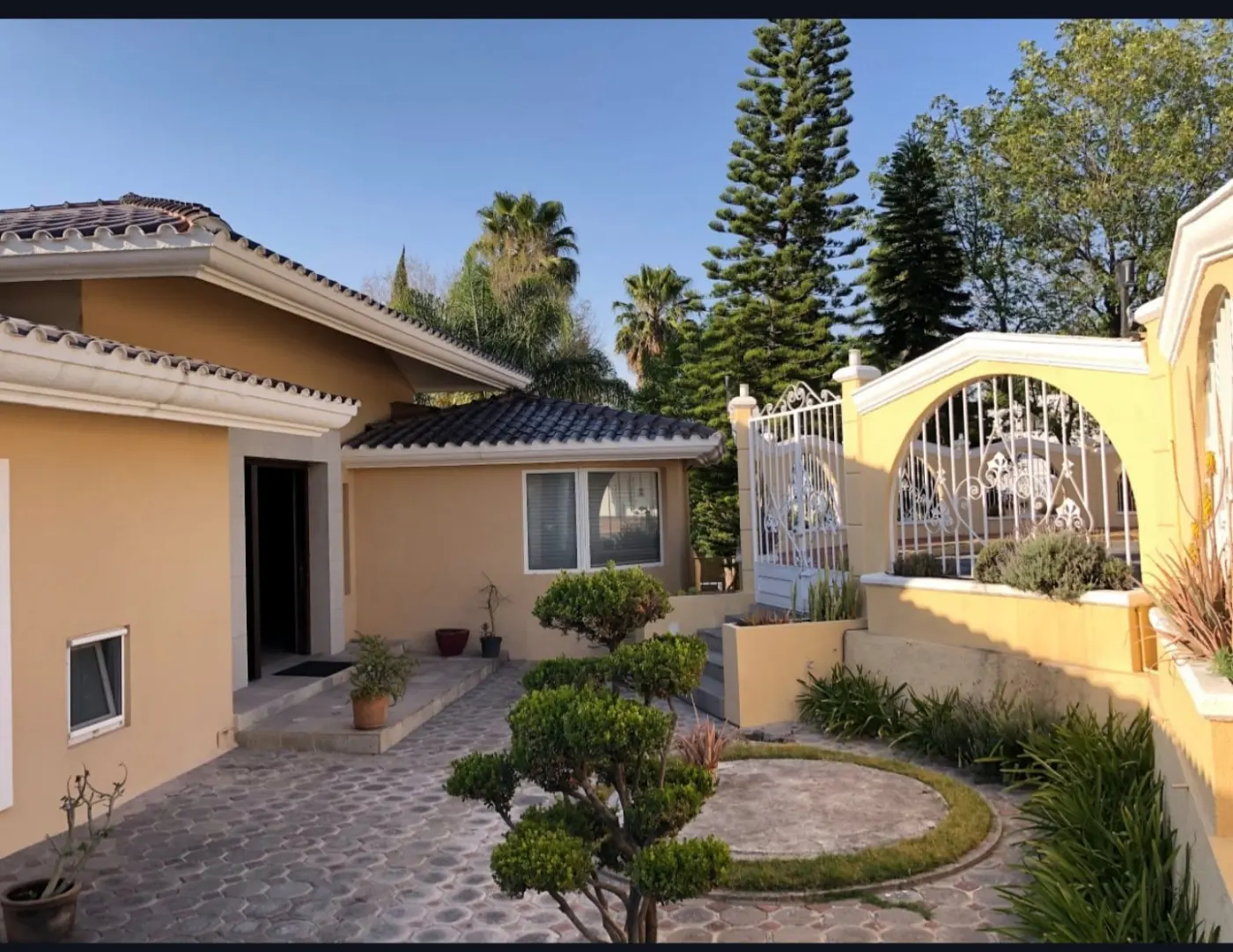 Fachada de la residencia, con cubierta de teja, jardín y reja de herrería blanca.