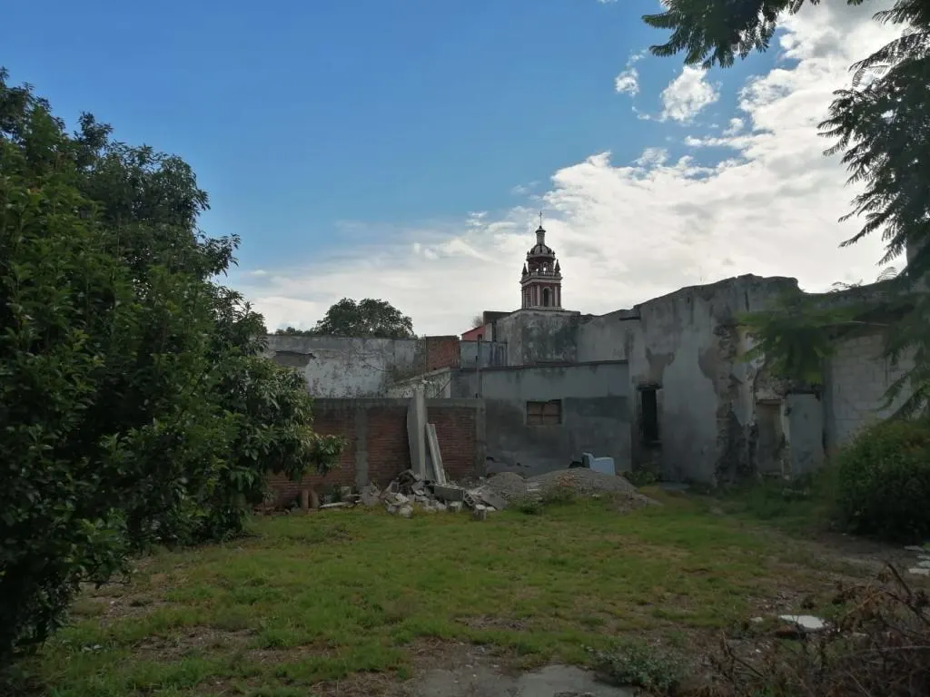 El terreno con los restos de una construcción de block y la iglesia del pueblo al fondo.