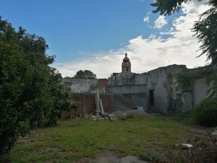 El terreno con los restos de una construcción de block y la iglesia del pueblo al fondo.